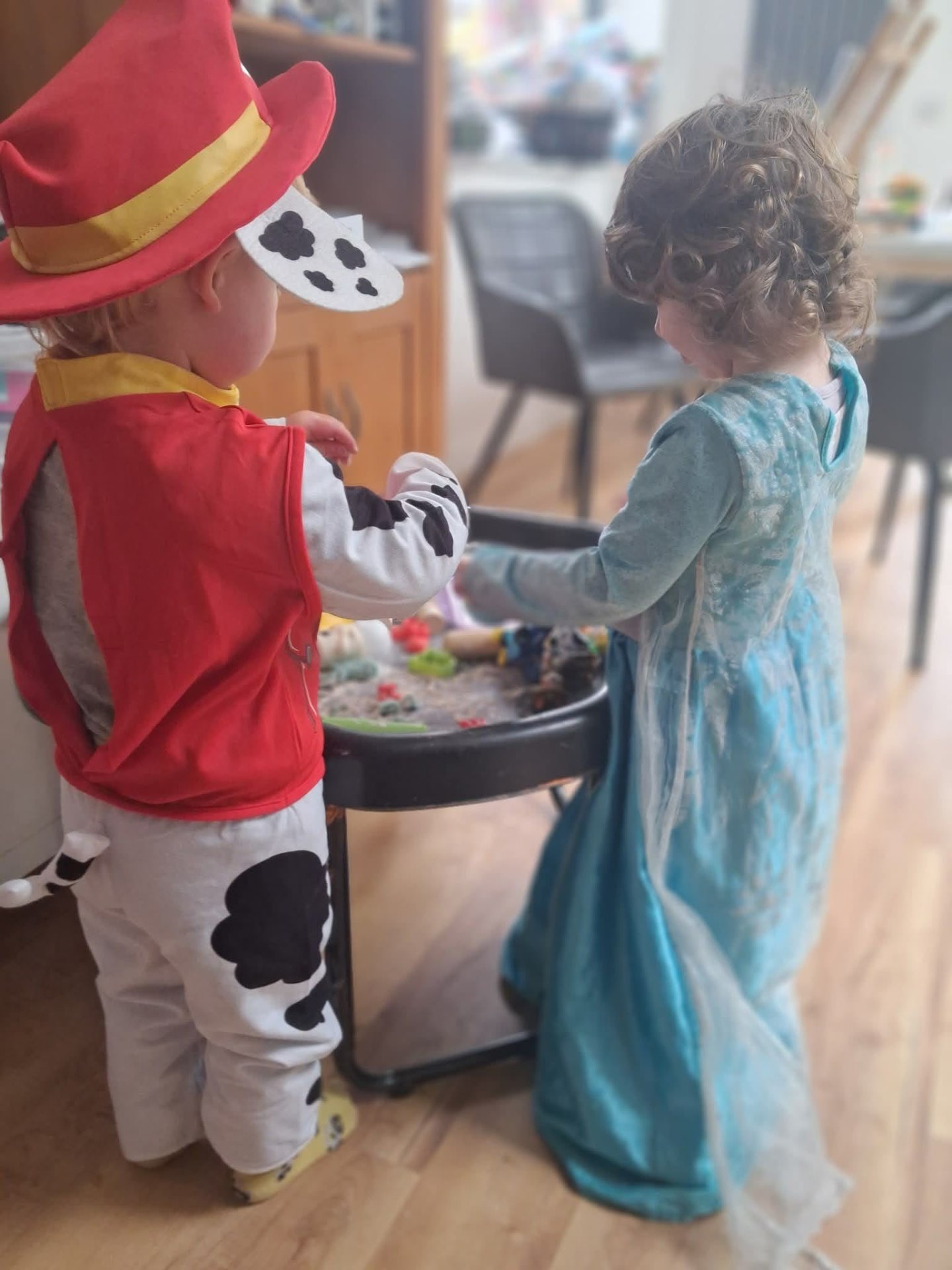 Two children in dressing-up costumes playing at the sand tray
