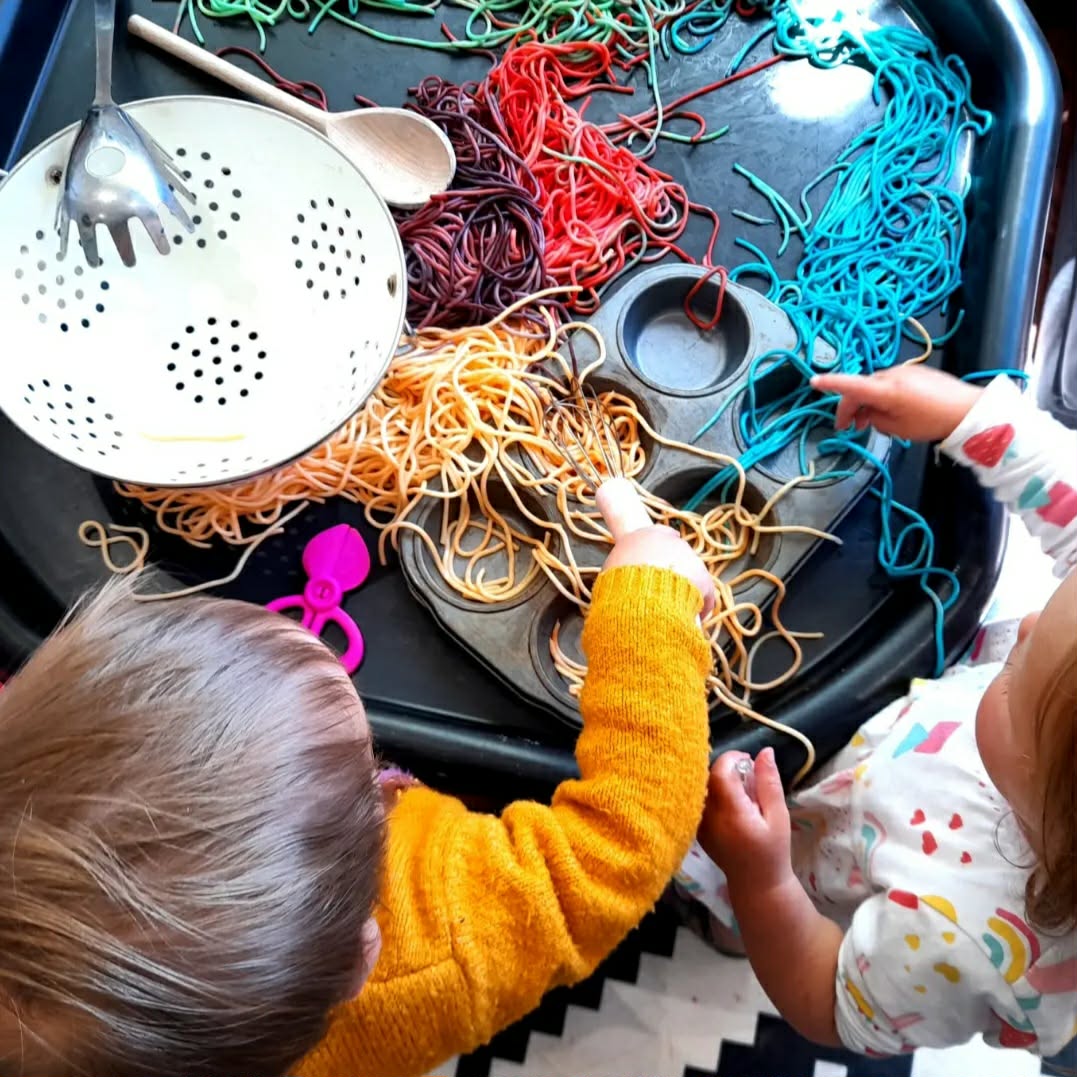 Toddlers exploring a colourful spaghetti sensory tray