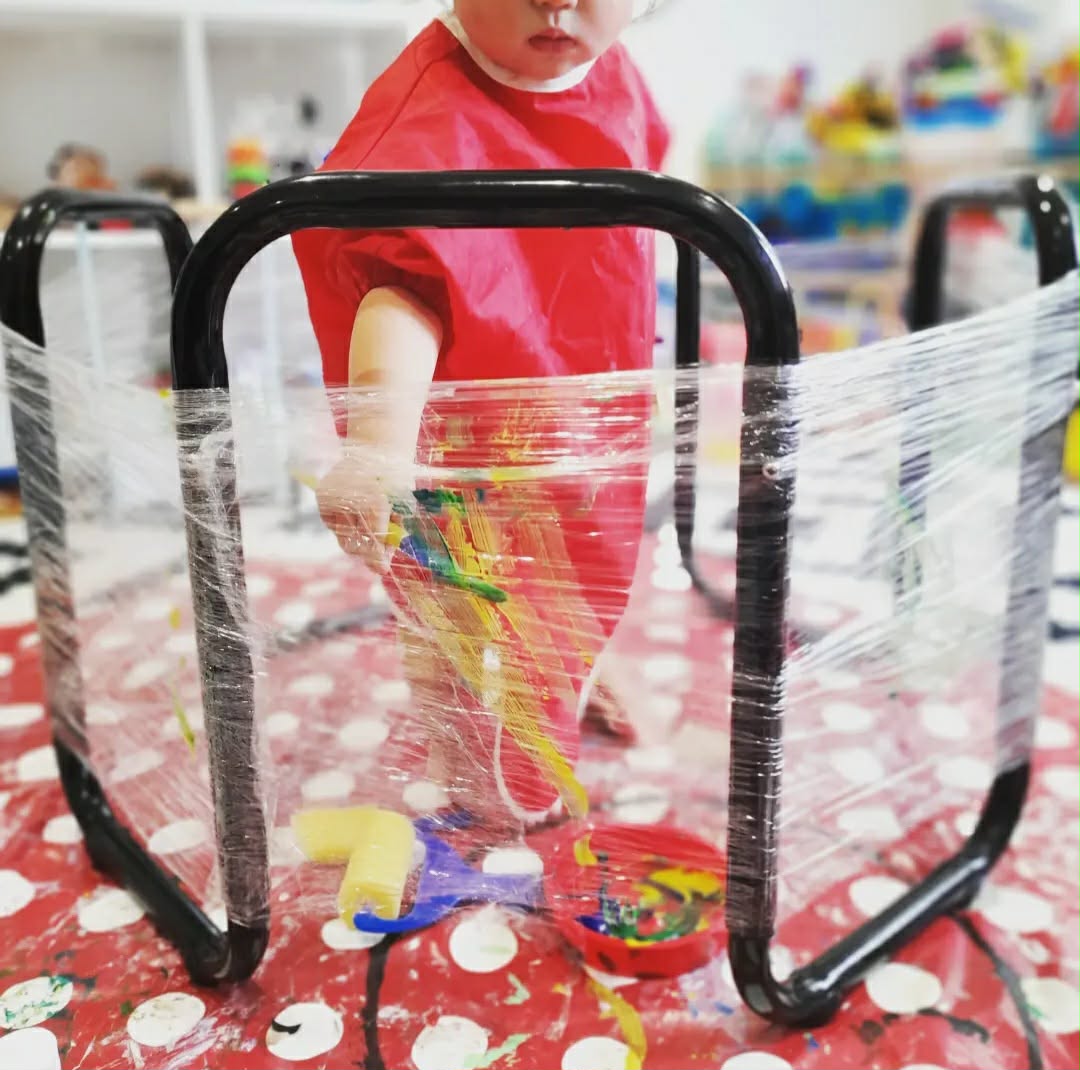Toddler finger painting behind a cling film screen