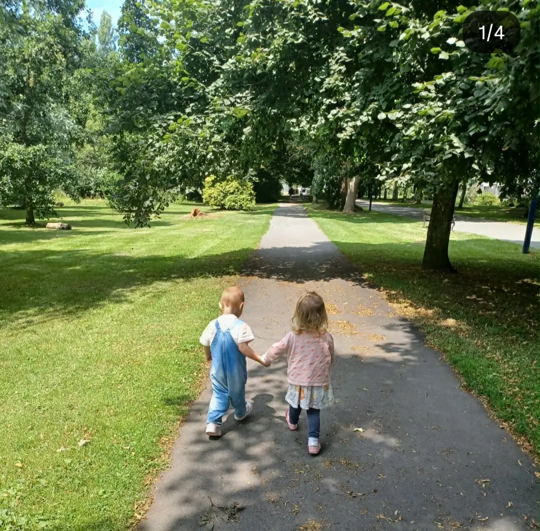 Two toddlers holding hands on a tree-lined park path