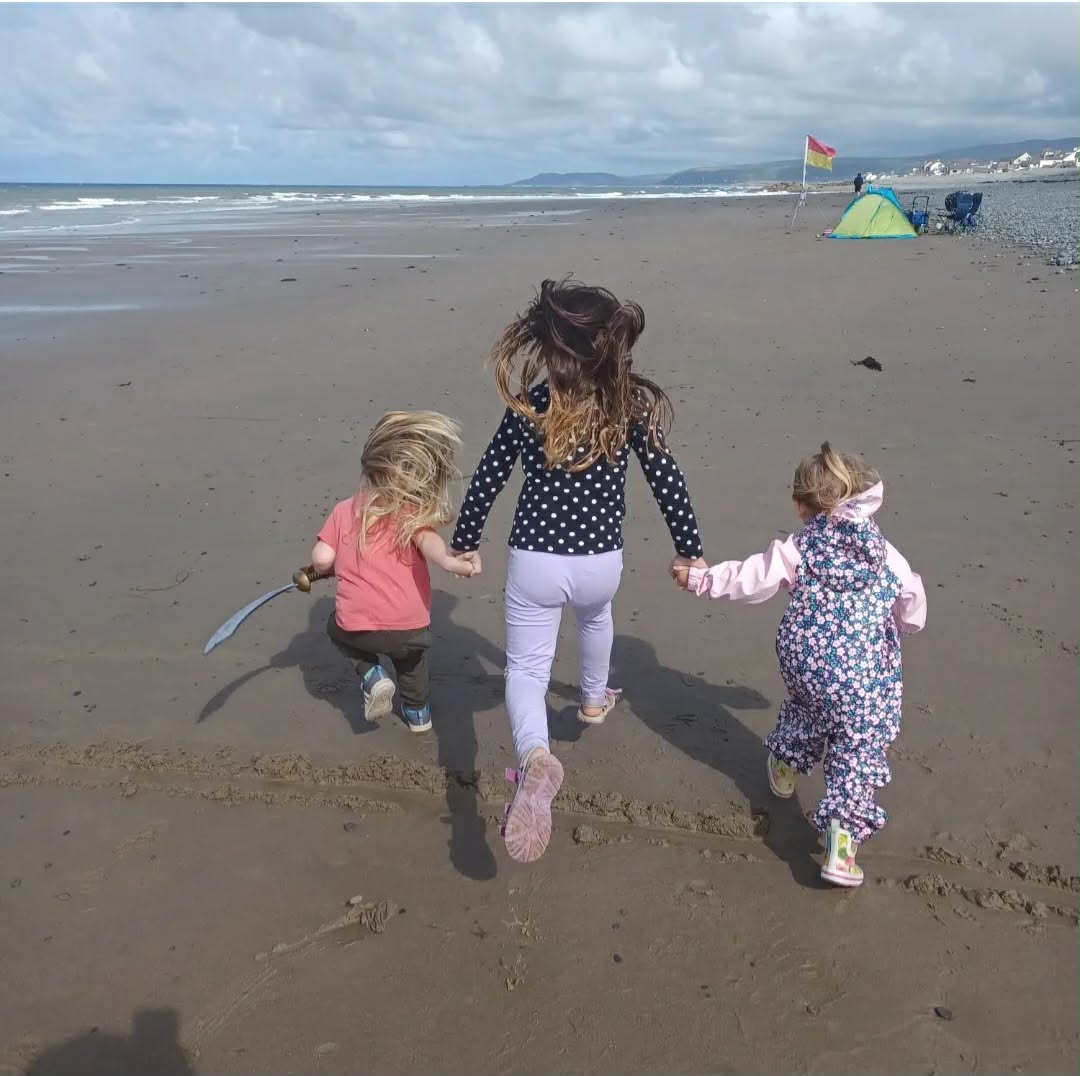 Three children running hand in hand along Borth beach