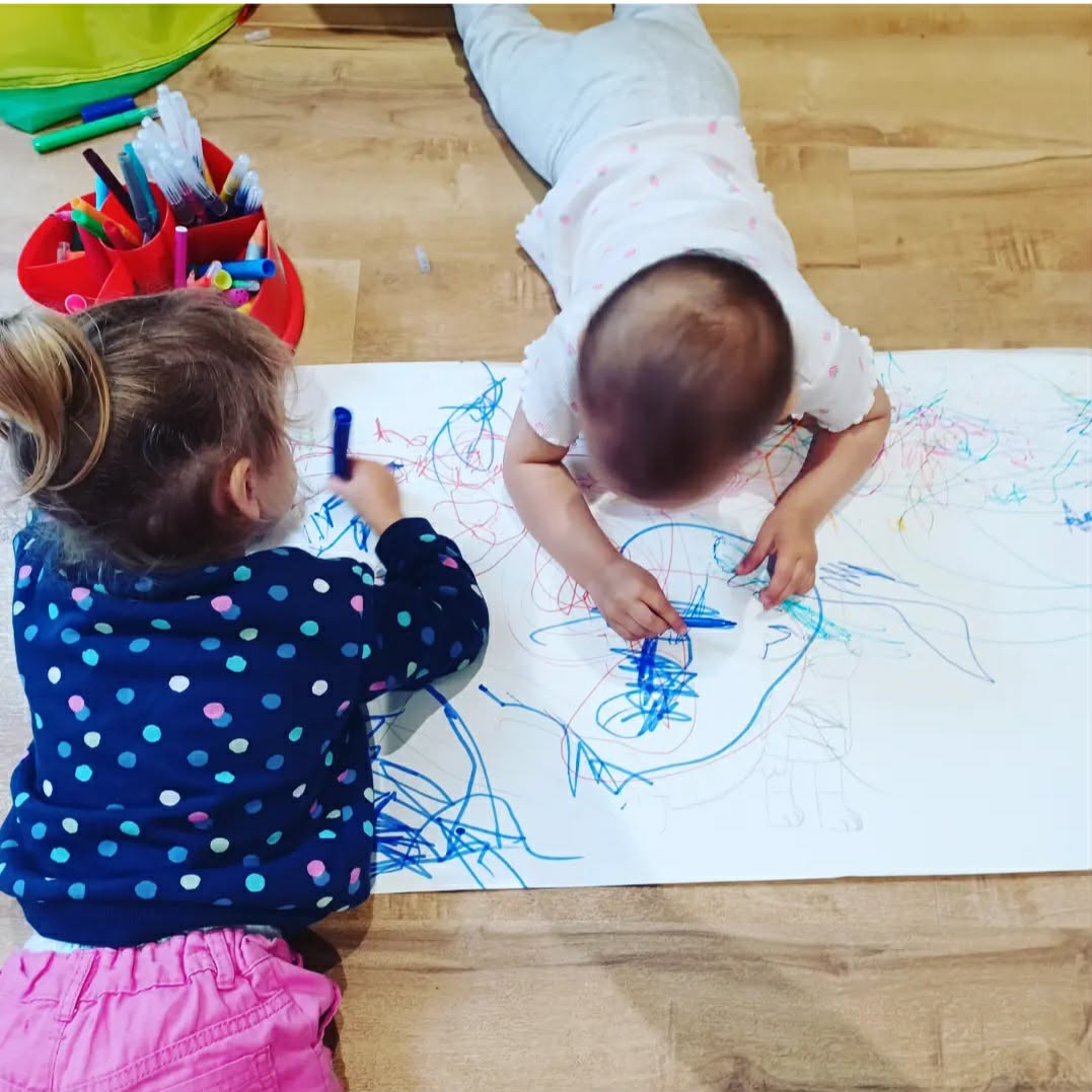 Two children drawing together on a big roll of paper